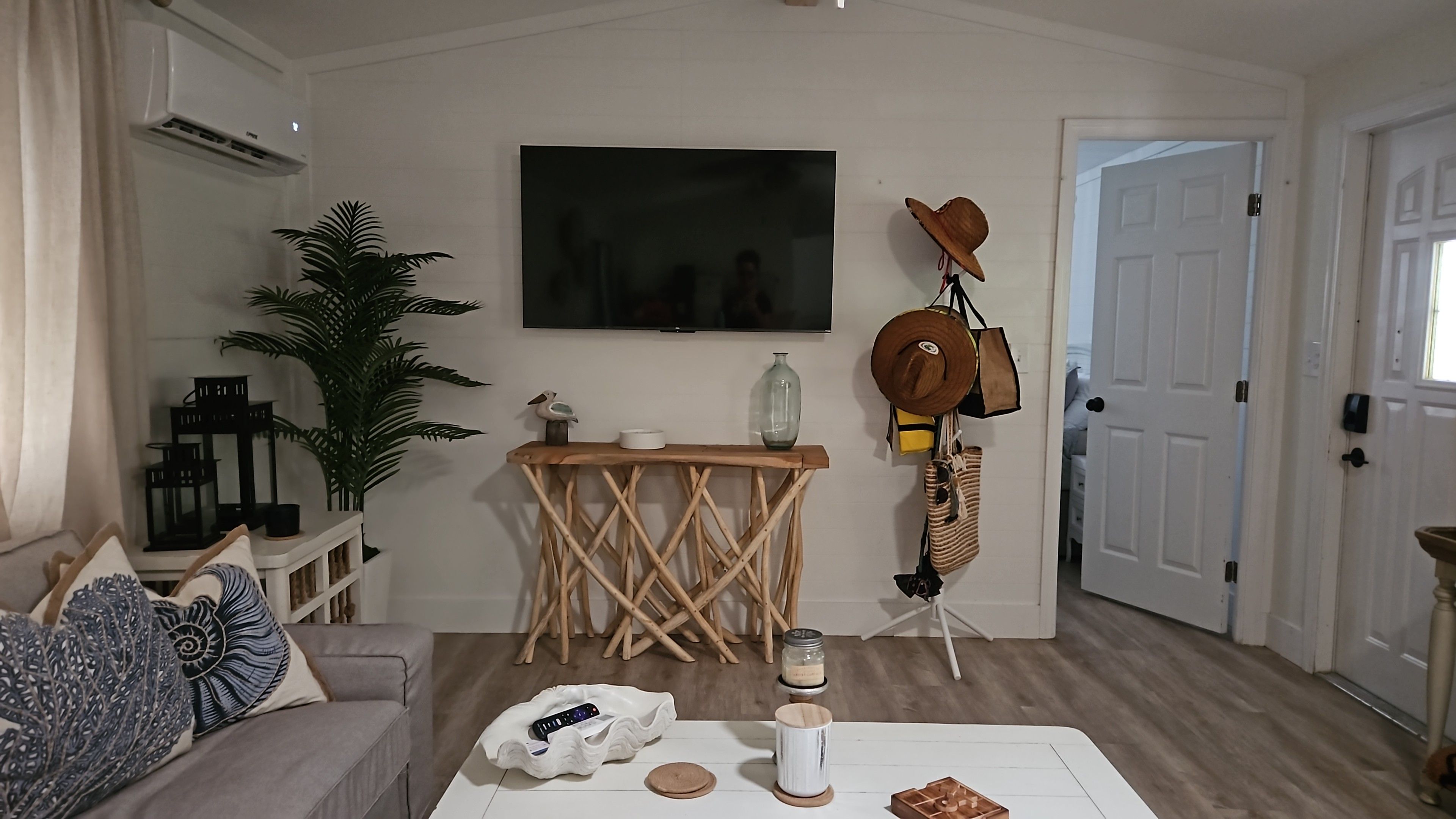 En stue med sofa, sofabord, fjernsyn, en plante og en dør.