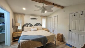 Un dormitorio con cama, mesitas de noche, ventilador de techo, aire acondicionado, armario y puerta.