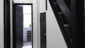 Un couloir doté d’un sol recouvert de moquette, d’un escalier noir et d’une porte donnant sur une pièce avec une fenêtre.