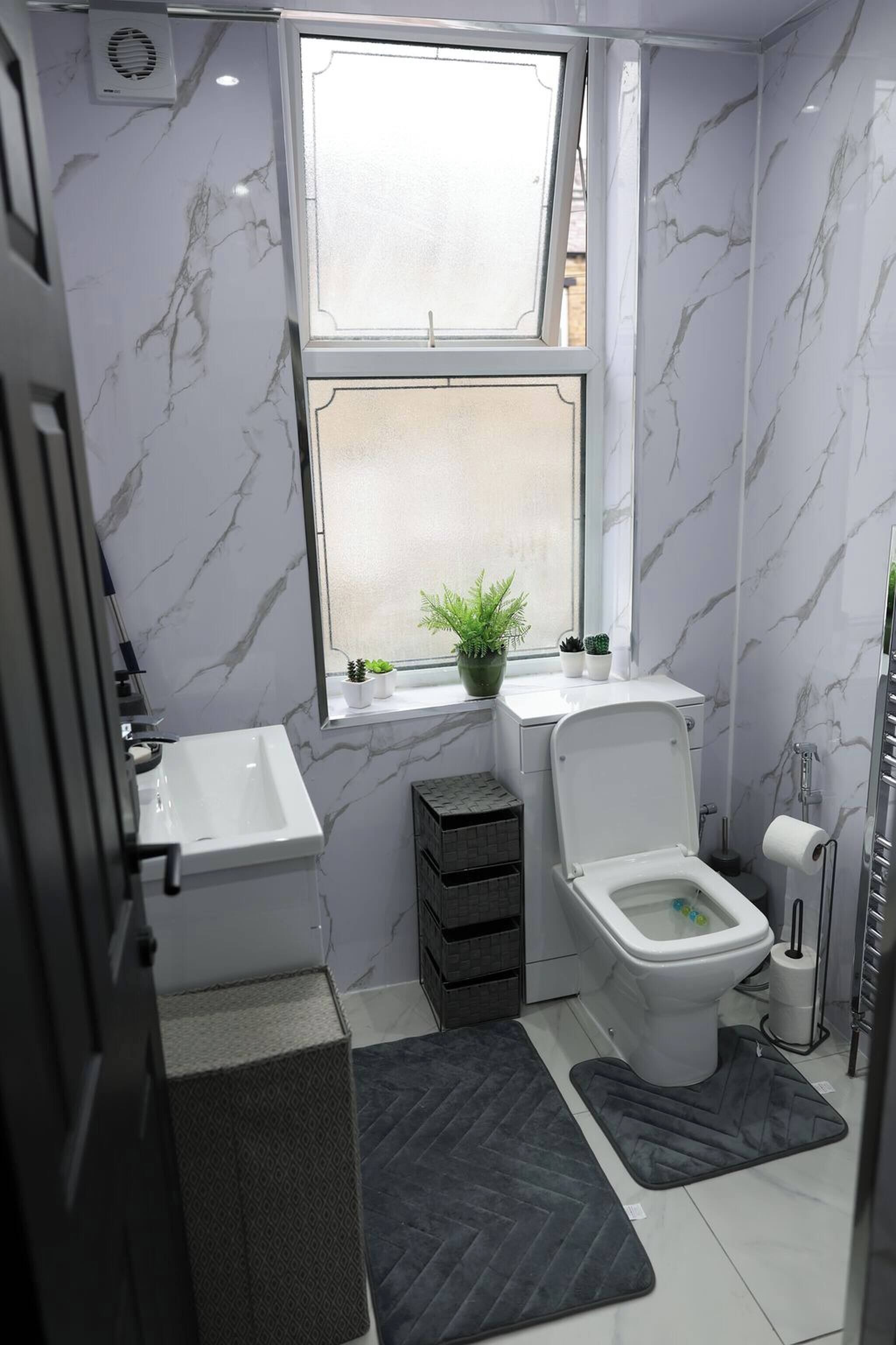 A bathroom with a toilet, sink, and window with plants.