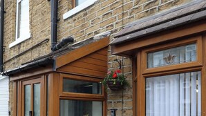 Une maison en briques avec une baie vitrée, une porte en bois et un petit jardin agrémenté de fleurs roses.