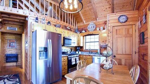 A wooden cabin interior with a kitchen featuring stainless steel appliances, a dining table with chairs, and a clock on the wall. - Hot Tub • Pet Friendly • 12 Min to Blue Ridge (Blue Ridge)