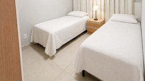 A hotel room with two single beds, a bedside table with a lamp, a wall-mounted air conditioner, and a ceiling light. - Apartment with balcony and sea view, 3 minutes from Atalaia beach. (Luís Correia)
