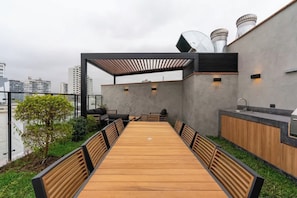 A rooftop terrace with a long wooden table, chairs, a small seating area, and a kitchen area. - Geko l Astounding 2BR w/ Parking in Miraflores (Miraflores)