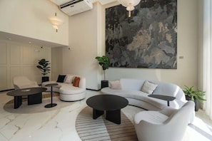 A modern living room with a white sofa, two black coffee tables, a large abstract painting, and a potted plant. - Geko | Stunning 1BR w/ Pool by the Malecón (Miraflores)