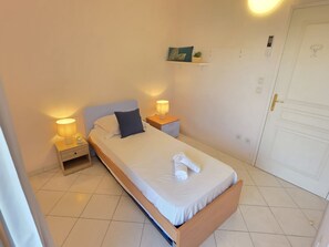A single bed with a wooden frame, two bedside tables with lamps, a white door, and a small shelf with a plant. - Villa Norma by Interhome (Cannes)