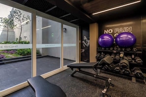 Ein Fitnessraum mit Trainingsgeräten, einer Bank und einer Wand mit dem Schriftzug 'NO PAIN'.