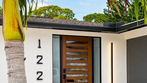 A modern house with a wooden door, numbered 1228, and a small garden with a palm tree.