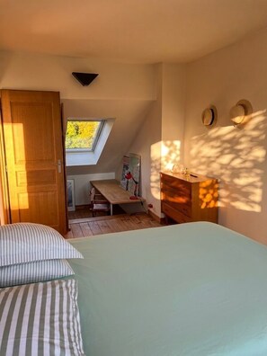A bedroom with a skylight, a wooden dresser, and a bed with striped bedding. - The Enclosed Garden of Cancale (Cancale)