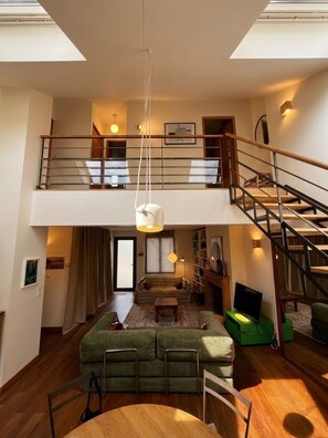 A spacious loft-style living area with a high ceiling, a staircase, and a mezzanine level. - The Enclosed Garden of Cancale (Cancale)