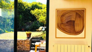 A room with a view of a garden, a wooden artwork on the wall, and a stone wall. - The Enclosed Garden of Cancale (Cancale)