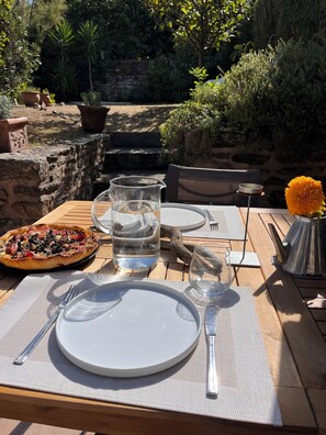 A table set outdoors with a pizza, a pitcher of water, and a vase with a flower. - The Enclosed Garden of Cancale (Cancale)