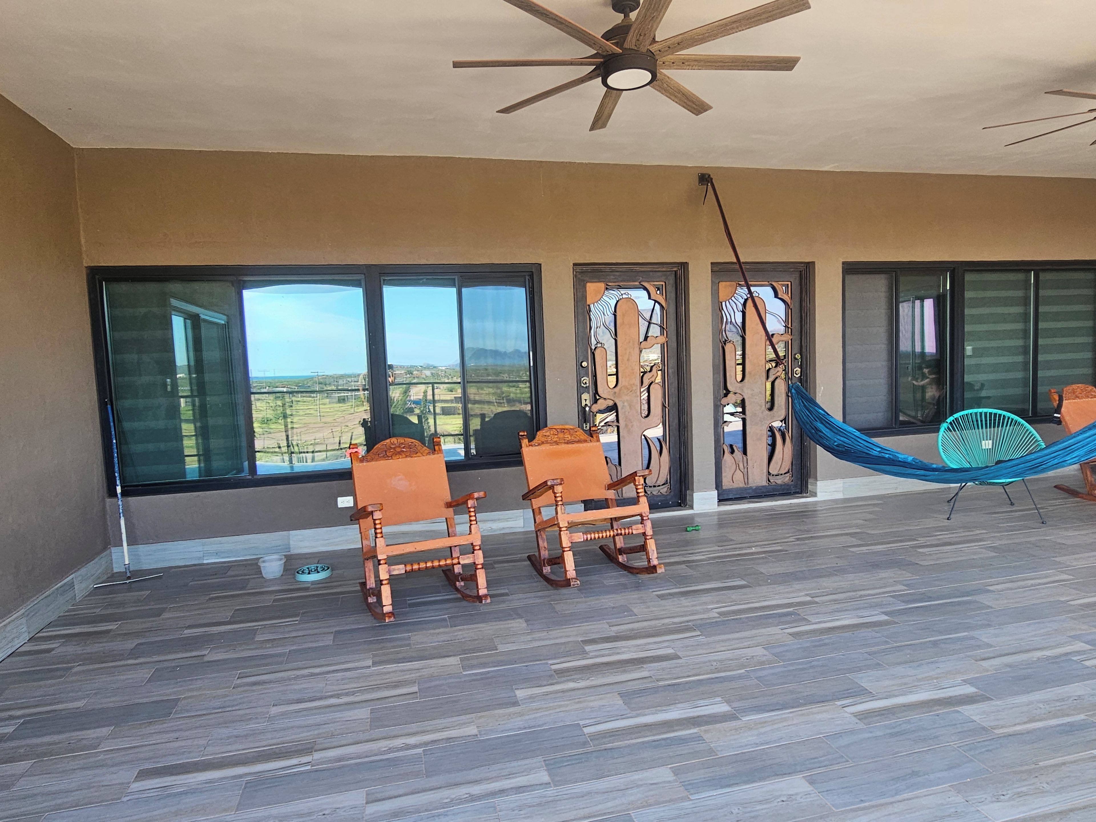 A room with a large window, a ceiling fan, and two rocking chairs.