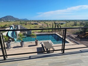 Un área de piscina con una cascada, rodeada de plantas en macetas y una terraza de madera.