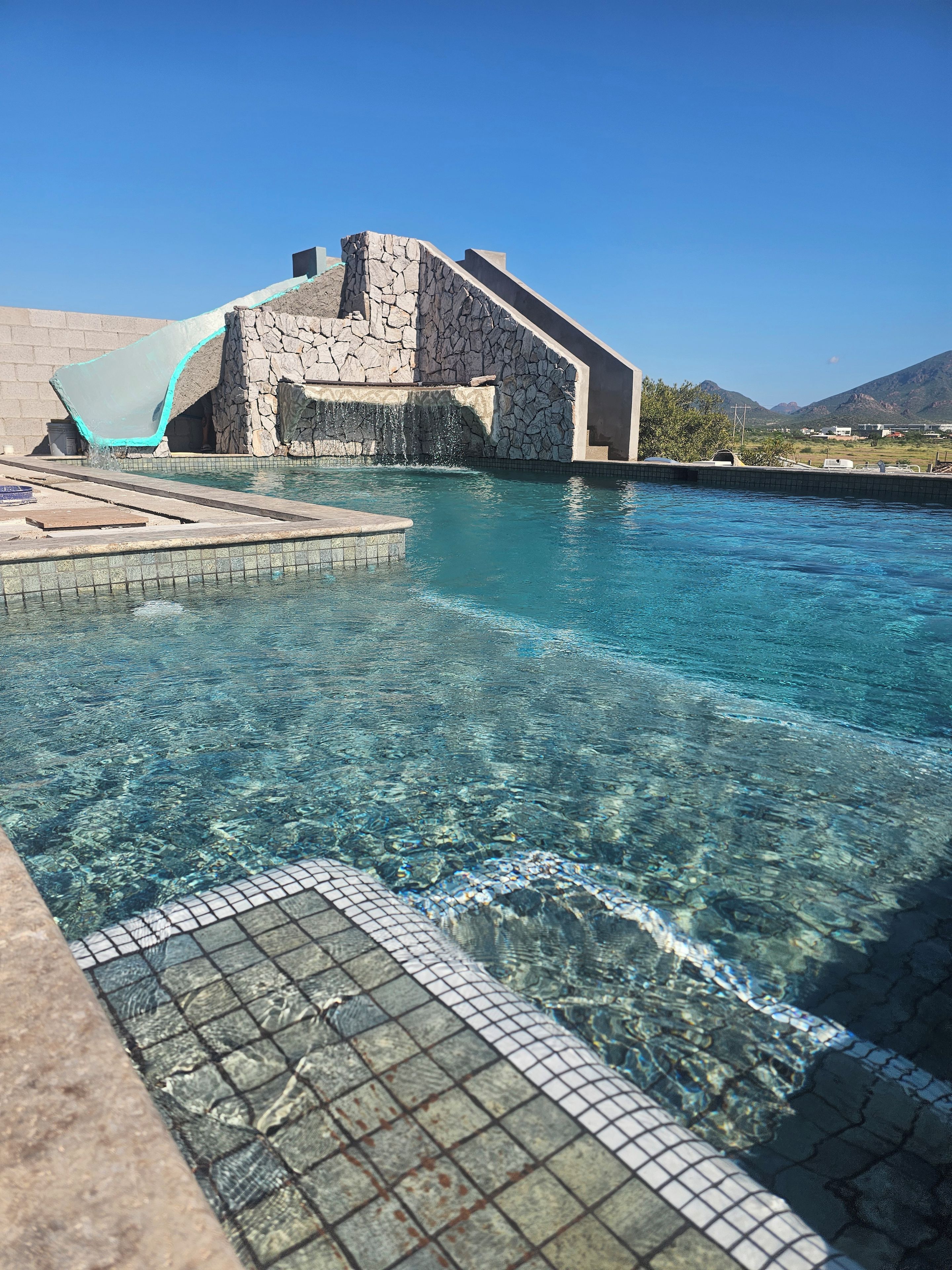 Una piscina nítida amb una paret de pedra i una cadira blava.