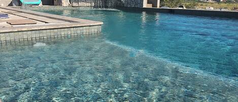 A clear pool with a stone wall and a blue chair.