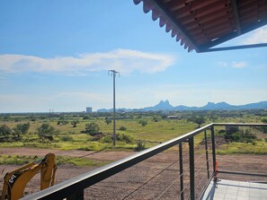 Vista desde un balcón cubierto sobre un paisaje rural con una cadena montañosa distante.