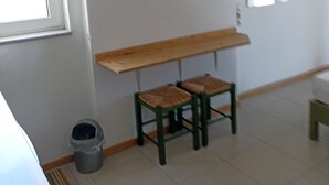 A room with a window, a wooden bench, two chairs, a small trash bin, and a tiled floor. - studio staring at sunset 1-bedroom studio in beautiful Χανια with AC (ΧΑΝΙΑ)