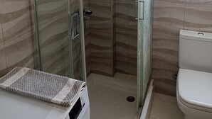 A bathroom with a glass shower enclosure, a toilet, and a sink with a towel. - studio staring at sunset 1-bedroom studio in beautiful Χανια with AC (ΧΑΝΙΑ)