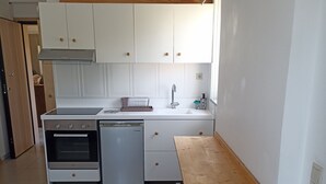 A compact kitchen with white cabinets, a built-in oven, a dishwasher, and a wooden dining table with a bench. - studio staring at sunset 1-bedroom studio in beautiful Χανια with AC (ΧΑΝΙΑ)