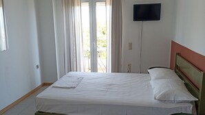 A room with a bed, a television on the wall, a window with curtains, and a ceiling fan. - studio staring at sunset 1-bedroom studio in beautiful Χανια with AC (ΧΑΝΙΑ)