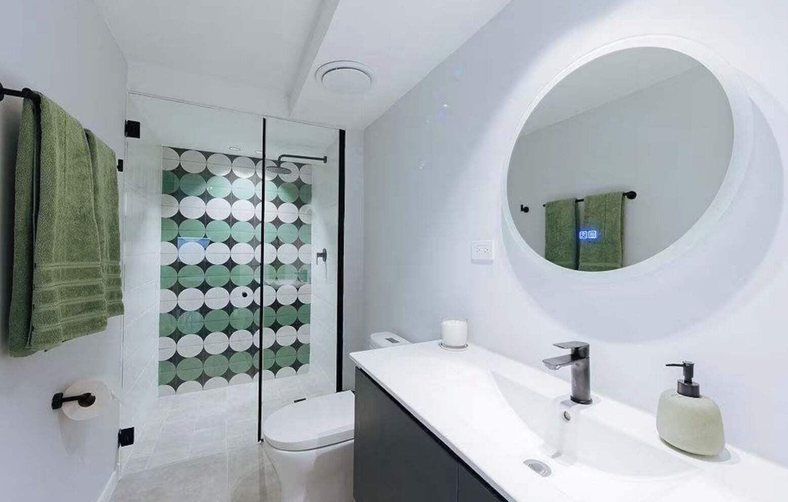Un bagno moderno con cabina doccia in vetro, uno specchio rotondo e un lavandino bianco.