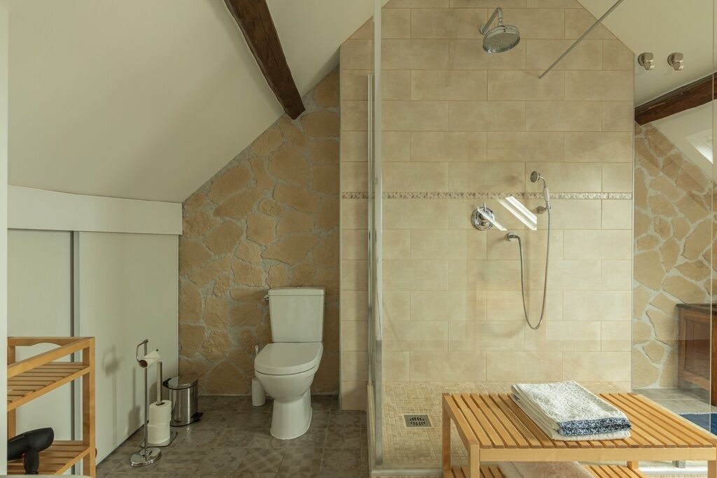 A bathroom with a shower, toilet, and a wooden bench.