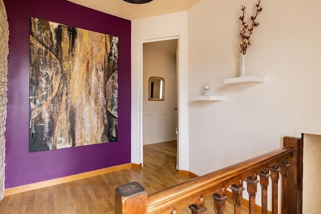 Una habitación con pared morada, escalera de madera y un cuadro abstracto grande.