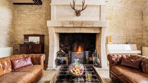 A room with a fireplace, leather sofas, a glass coffee table with decorative items, and a mounted deer head.