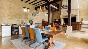 Un comedor rústico con una mesa de madera, sillas azules y anaranjadas, y lámparas colgantes.