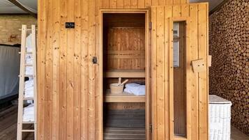 Uma sauna de madeira com a porta aberta, mostrando prateleiras com toalhas e uma pequena estante com um pote.
