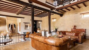 A spacious living area with a leather sofa, wooden beams, stone walls, and a staircase.