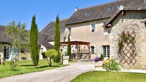 A stone building with a covered porch, a stone wall with climbing plants, and a well-maintained lawn.