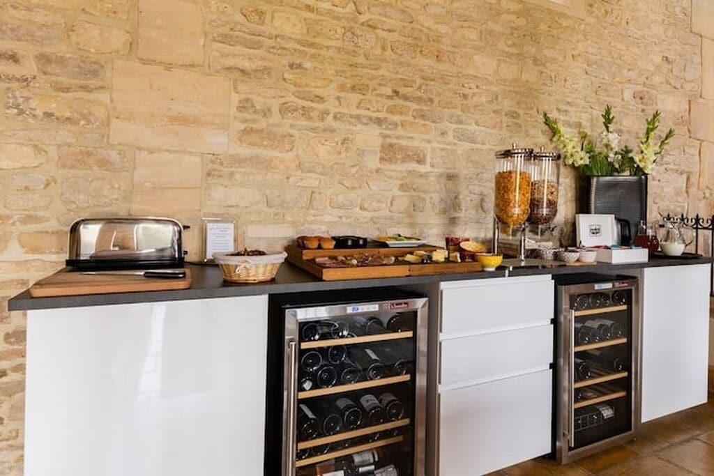 Una cocina con pared de piedra, un tostador, una cesta de pan, un frutero, un refrigerador de vinos y una máquina de café.