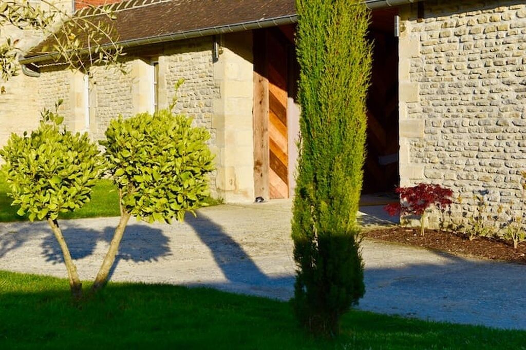 A stone building with a gravel driveway, a wooden door, and a small tree in the foreground.