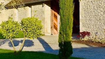 A stone building with a gravel driveway, a wooden door, and a small tree in the foreground.