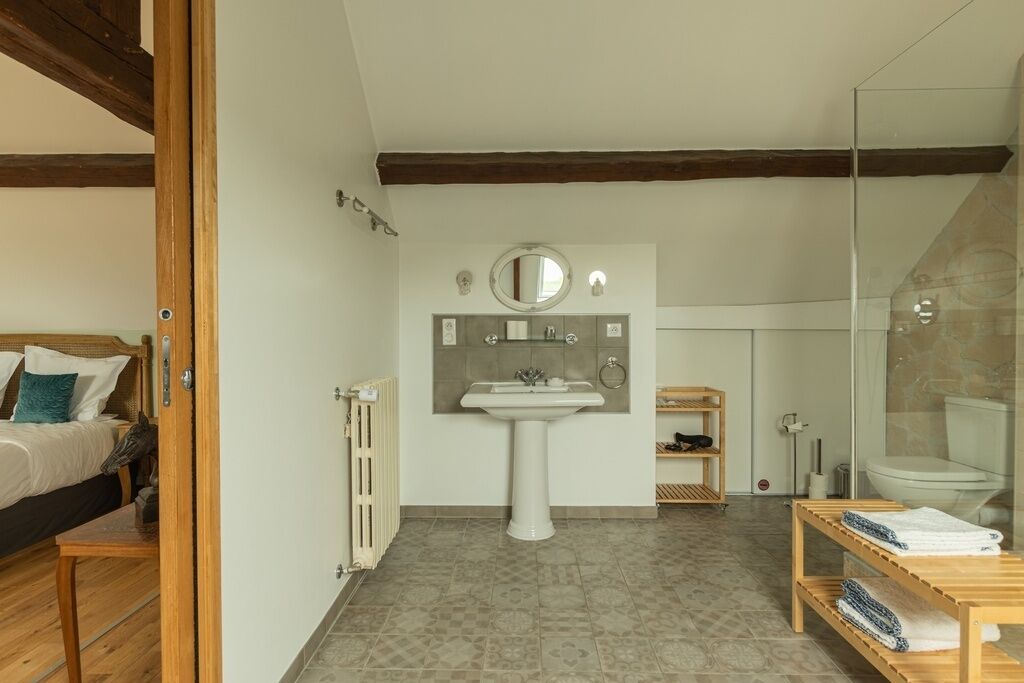 Une chambre à coucher comprenant un lit, une table de chevet et un radiateur, ainsi qu’une salle de bain avec un lavabo, un miroir et des toilettes.