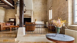 Una habitación amplia con chimenea de piedra, sofá de cuero, una mesa de comedor con un jarrón de flores y una escalera que conduce a un nivel superior.
