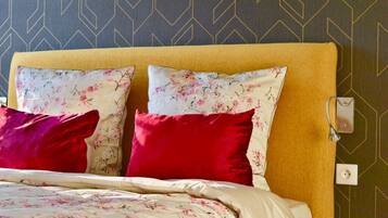 Una cama con ropa de cama floral, almohadas rojas y blancas y una pared con diseño geométrico.