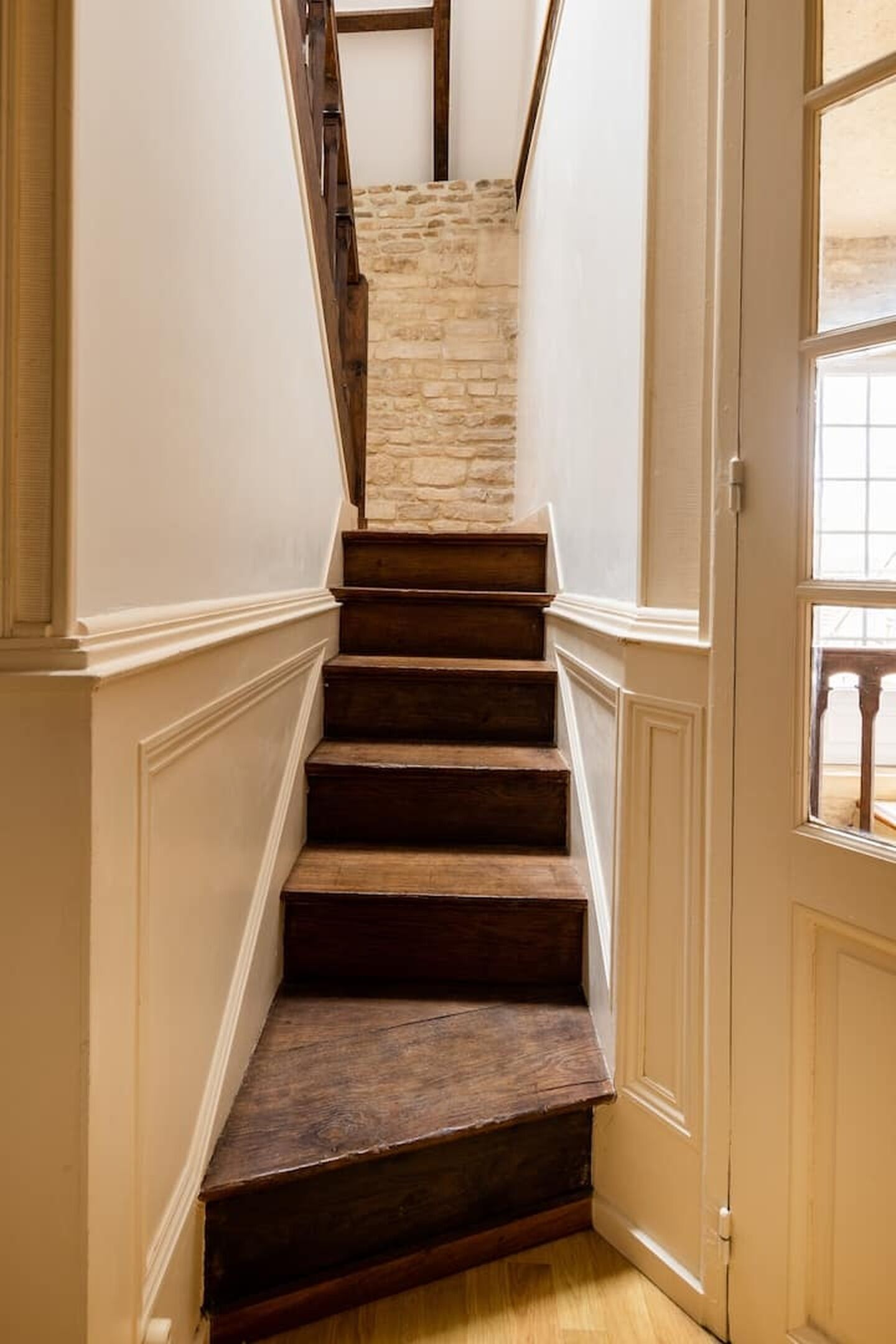 A staircase with wooden steps leading to a stone wall, white walls, and a door with a window.