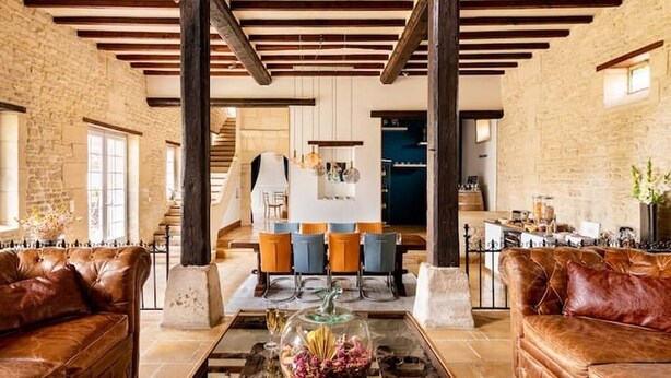 A spacious living area with leather sofas, a glass coffee table, and a kitchen in the background.
