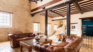 Una habitación amplia con un sofá de cuero, una mesa de centro y una escalera que sube a otro nivel.