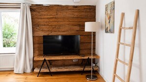 Een kamer met een houten wand, een flatscreen televisie op een houten voetstuk, een vloerlamp en een ladder.