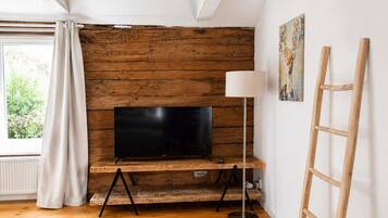 Habitació amb paret de fusta, televisió de pantalla plana sobre un suport de fusta, làmpada de peu i una escala.