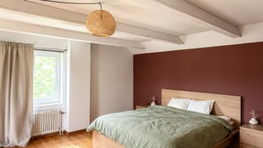 Een slaapkamer met een houten bed, een raam met gordijnen, een radiator en een hanglamp.