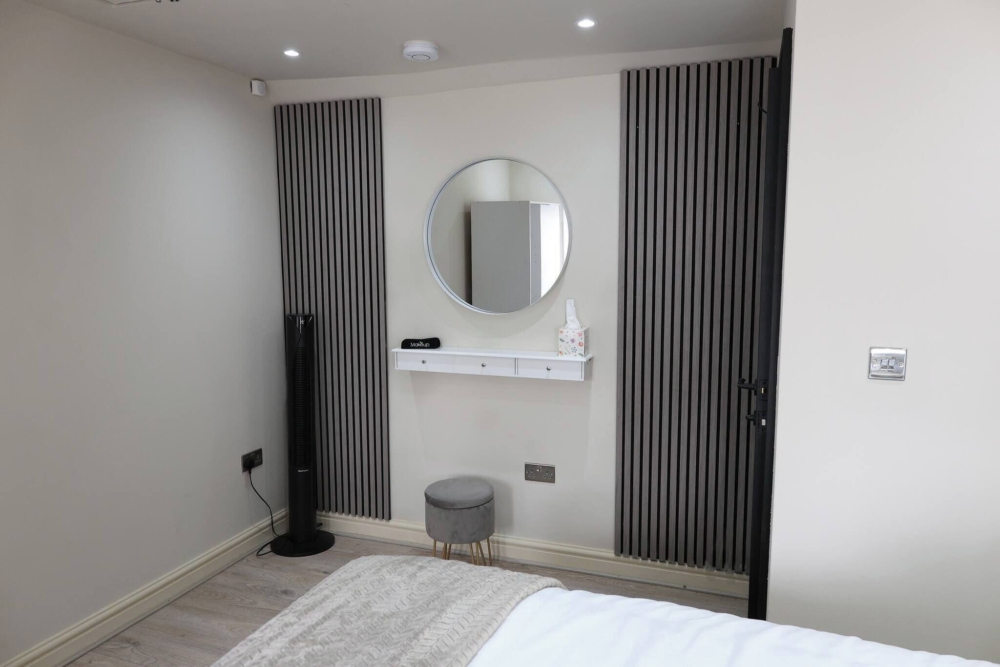 A bedroom with a bed, a round mirror, a small stool, and a radiator.