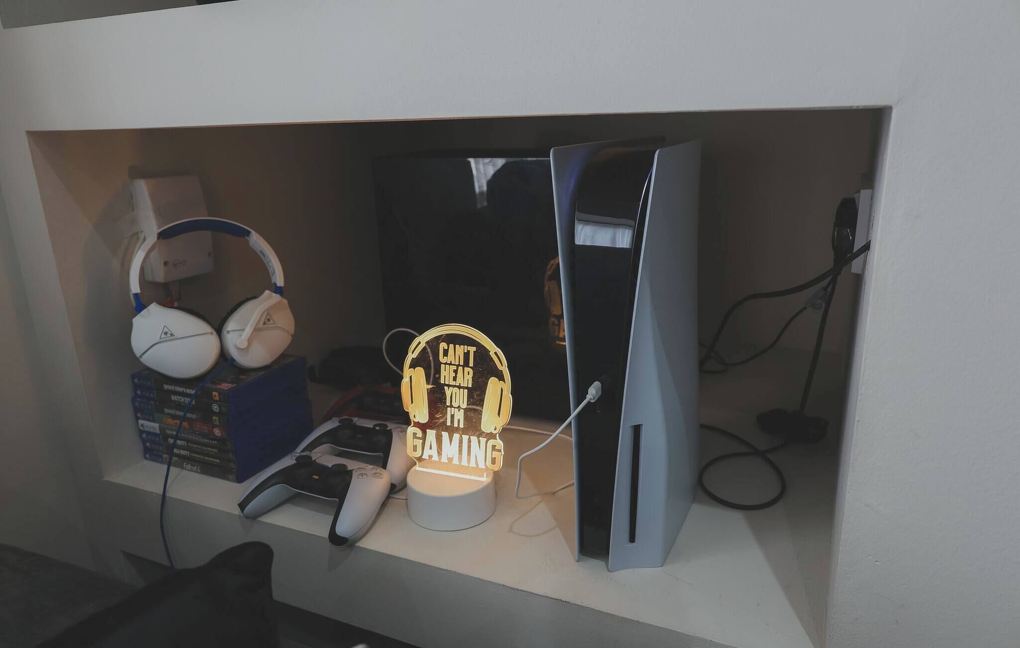 Una configuración para juegos con un letrero de neón, audífonos, una consola de videojuegos y una estantería.