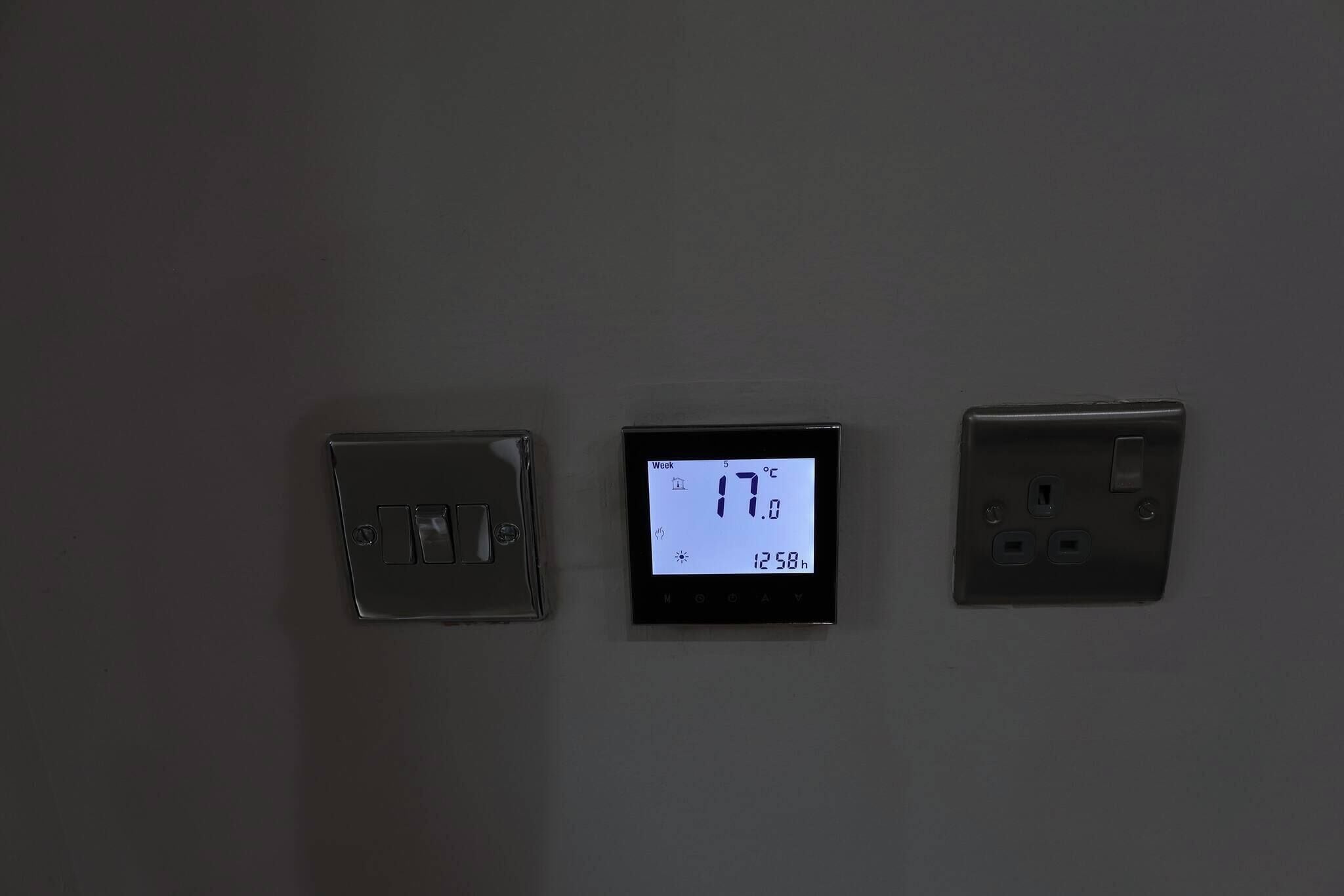 A thermostat, a digital clock, and a power outlet on a wall.