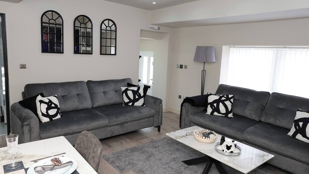 A living room with two grey sofas, a coffee table, and a dining area with a table set for two. - White Bungalow With 75" Tv, Air Con, Contractors (Bradford)