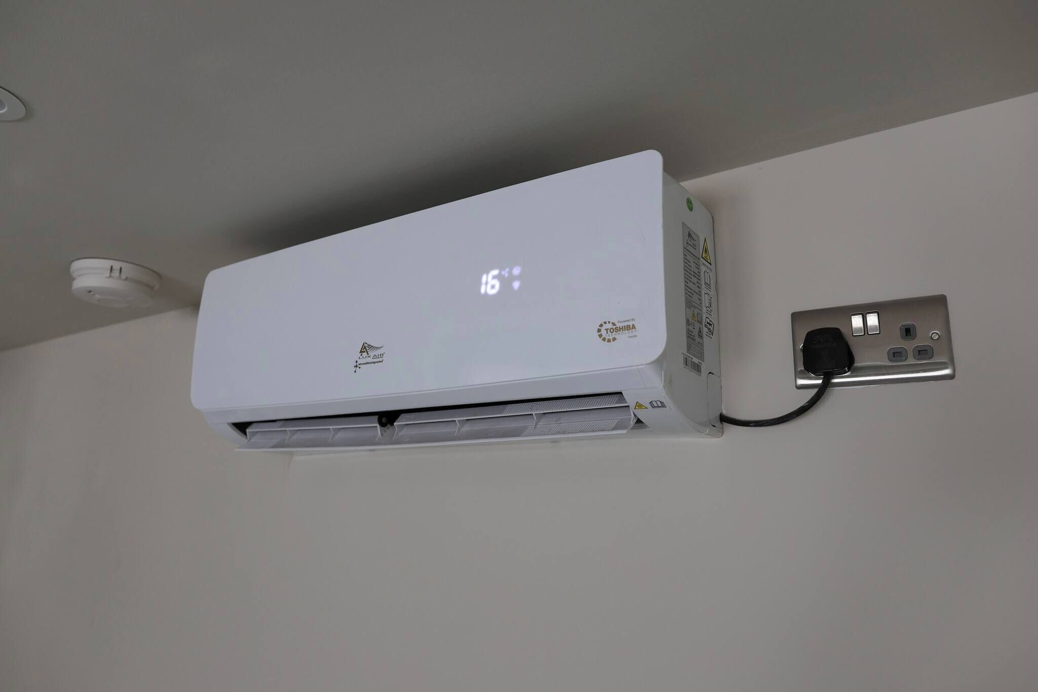 A white air conditioning unit mounted on a wall with a digital display showing 16 degrees.